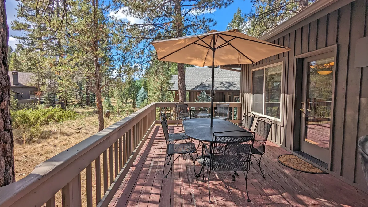 A tranquil outdoor dining area with a large table, umbrella, and lush trees in the background. The setup is ideal for relaxing, socializing, or sharing a meal after a walk or play session in the park.