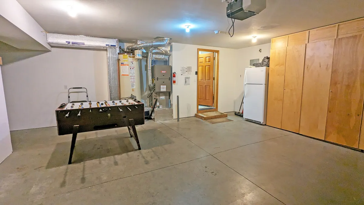 This interior image centers around a foosball table set in the garage, with adjacent wooden cabinets, a refrigerator, and a doorway in the background. The scene conveys a playful area designed for informal gatherings and spontaneous entertainment.