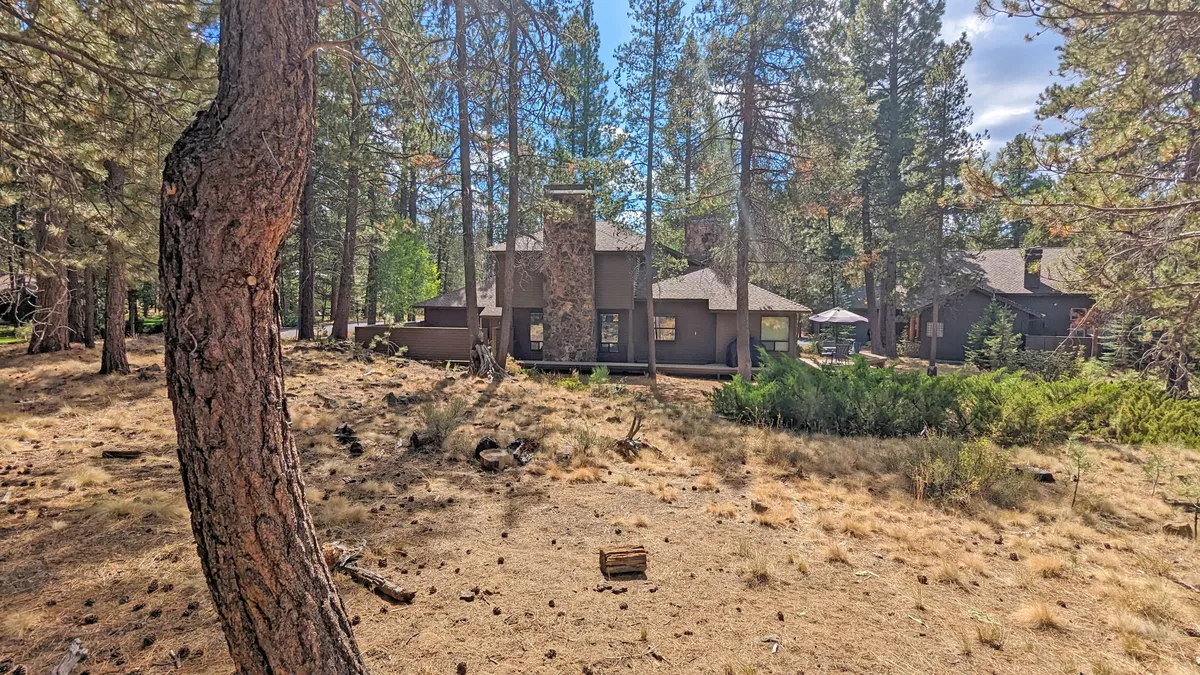 A broad exterior shot of the home nestled among tall trees, with a stone chimney and inviting porch, evoking a sense of arrival and connection to the natural landscape.
