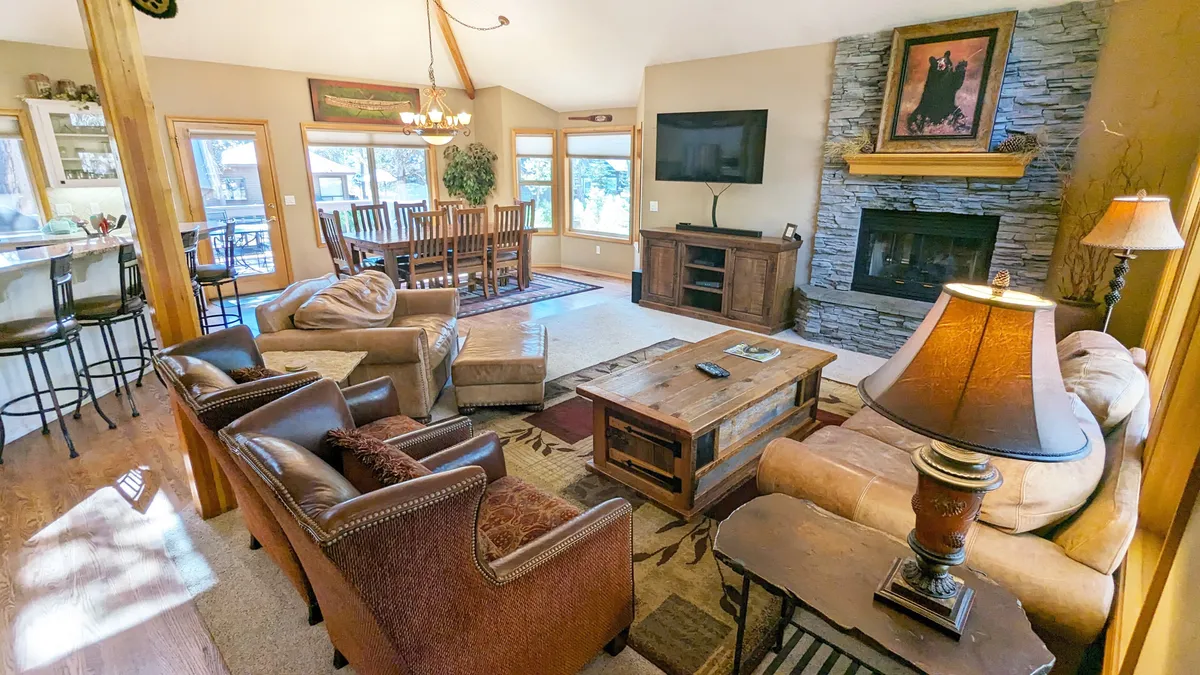 A warmly lit living and dining area featuring a striking fireplace, cozy comfortable seats, a prominent solid wood dining table, and decorative artwork. The ambiance is intimate and comforting, ideal for evenings by the fire or shared meals.