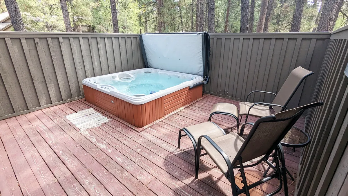 This image showcases a tranquil outdoor deck surrounded by trees, featuring a private hot tub and seating area. The space is set for relaxation or socializing in a serene natural environment, highlighting the opportunity for guests to unwind after a day of adventure.