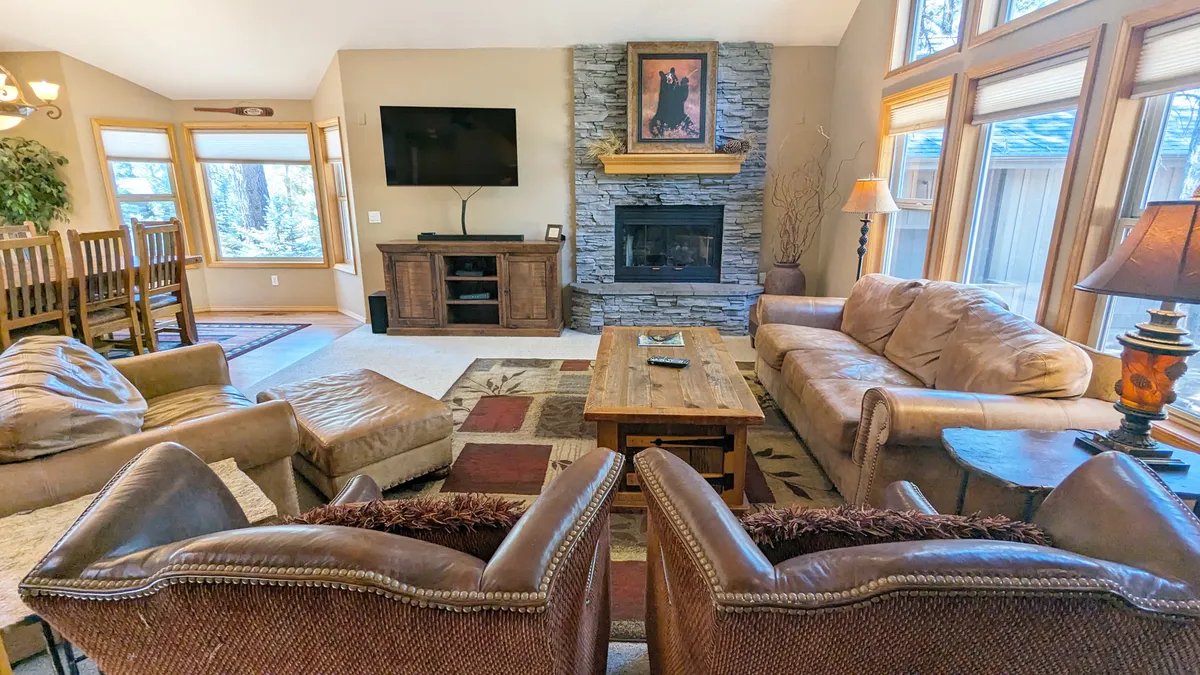 A welcoming living room with a fireplace, large windows, plush seating, and a wooden coffee table, exuding a cozy, communal atmosphere ideal for relaxing with pets and family.