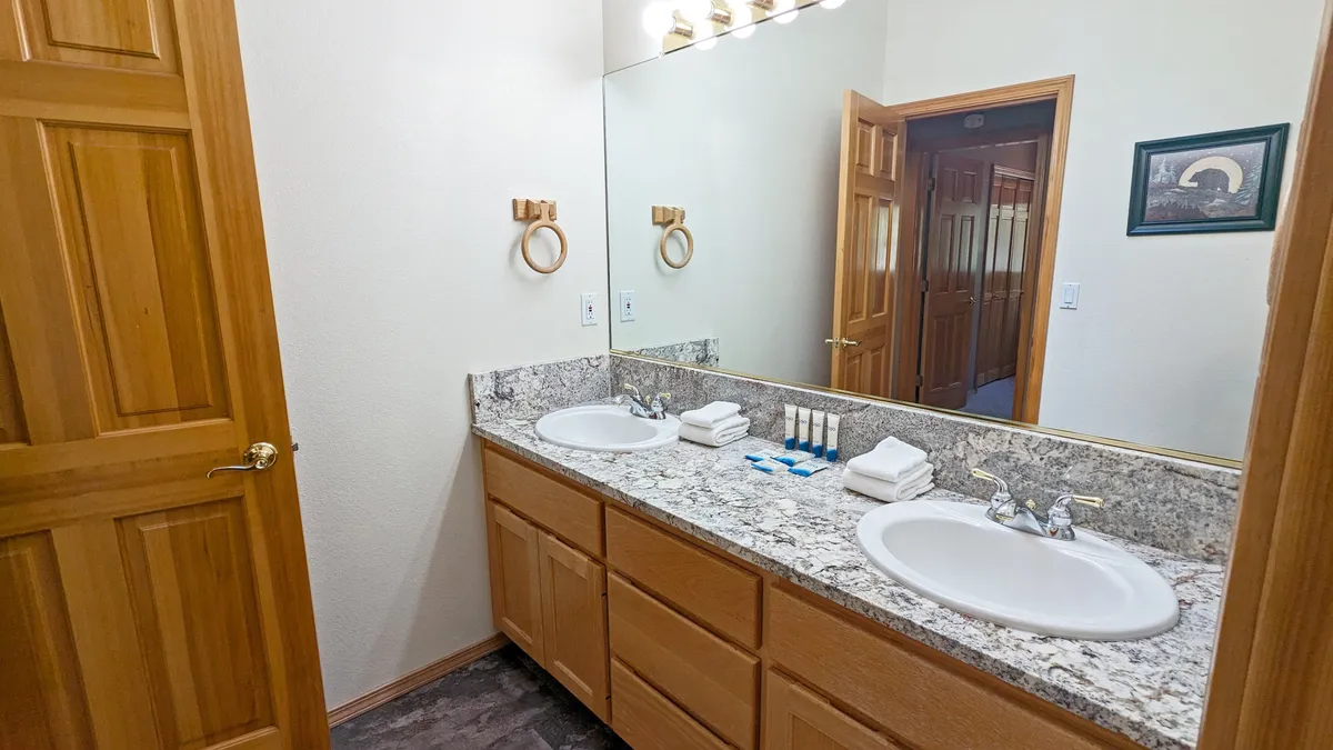 A modern bathroom with a double sink vanity, granite countertop, large mirror, and wooden door, exuding a sense of calm organization perfect for unwinding or starting the day refreshed.