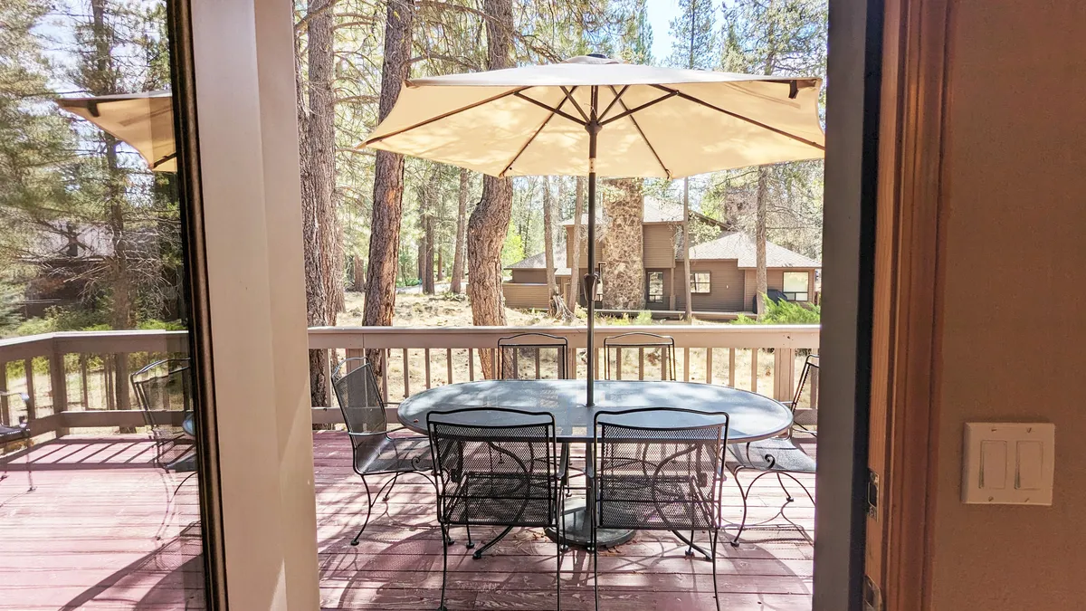 A tranquil outdoor deck with a dining table, parasol, and surrounding trees, offering direct access to nature for both people and pets.