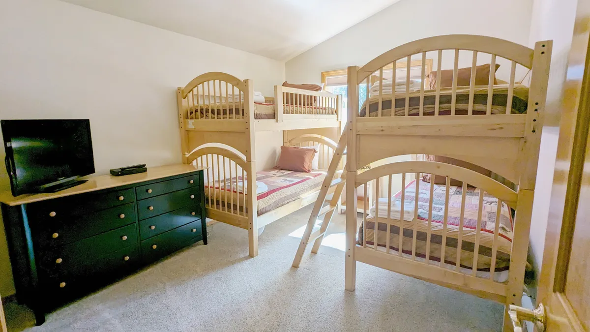 A playful and inviting bunk room with two sets of bunks, a dresser for storage, and a television for entertainment. The space feels warm and comfortable, ideal for children or group sleepovers.