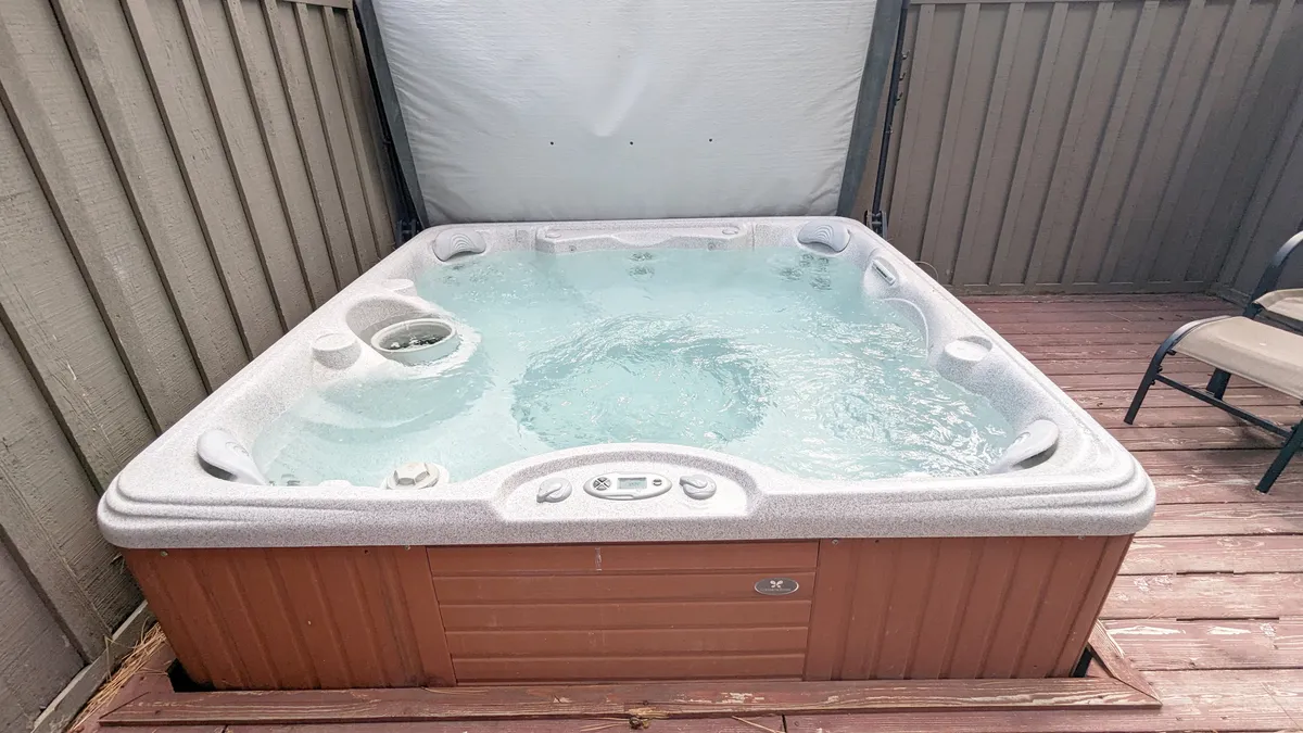 A serene hot tub set on a wooden deck, flanked by privacy walls and surrounded by nature. The scene evokes a spa-like atmosphere, ideal for relaxing and unwinding after an active day outdoors.
